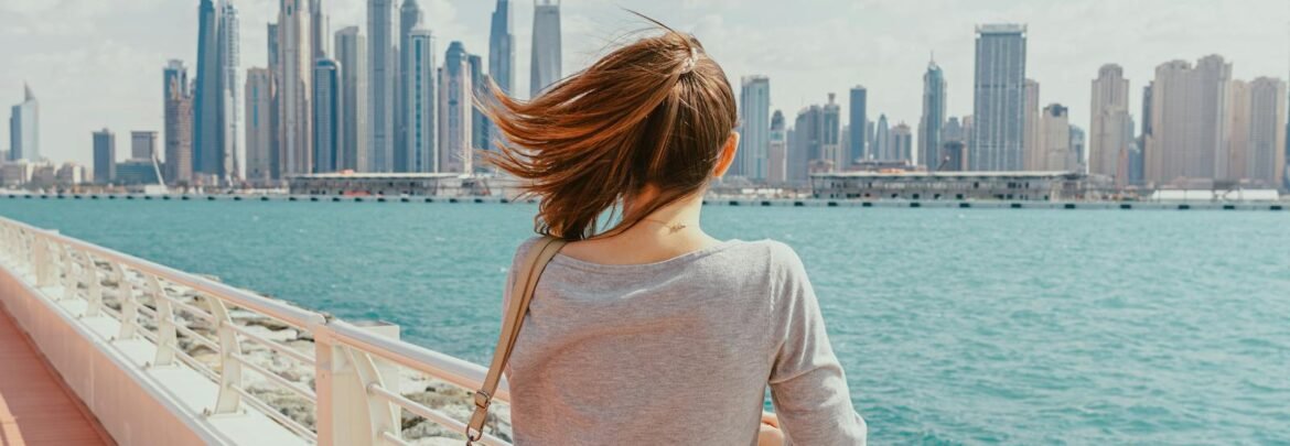 Woman gazes at Dubai Marina's modern skyline from a waterfront promenade.